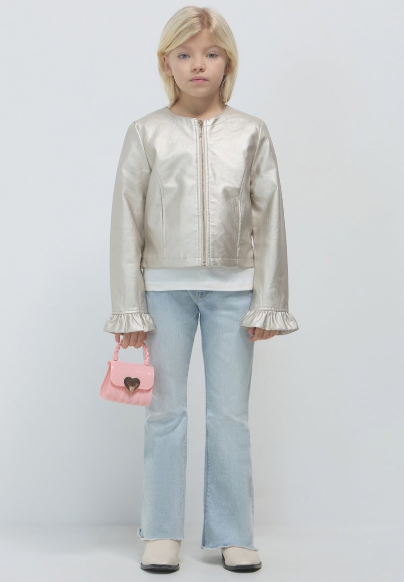 Giacca bomber metallica argento con maniche a campana, indossata sopra un top bianco. Abbinata a jeans svasati azzurri chiari e una piccola borsa rosa.