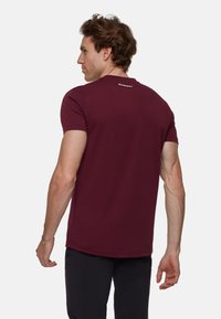 Bordowa koszulka z krótkim rękawem, wykonana z miękkiego materiału. Posiada okrągły dekolt oraz małe białe logo na plecach. Gładka tekstura i dopasowany krój.