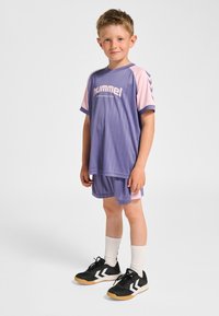 Lila och rosa sportuniform med ränder; inkluderar en kortärmad tröja och shorts. Svarta skor med vita detaljer och texturerade sulor.
