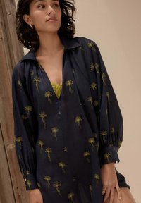 Marineblauwe blouse met gele bloemenborduurwerk, voorzien van een diepe V-hals en lange mouwen met knoopmanchetten. Zachte, gestructureerde stof.