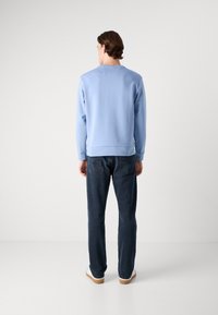 Light blue sweatshirt with ribbed cuffs and hem, paired with dark blue straight-leg jeans. Smooth fabric, minimal design.