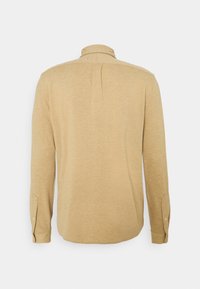 Koszula z długim rękawem w odcieniu beżowym z delikatną strukturą, z zapięciem na guziki przy kołnierzyku i mankietach. Widok z tyłu ukazuje detal w postaci centralnego plisowania.