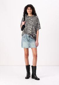 Oversized t-shirt med leopardmönster, blekt denim minikjol, svarta knähöga stövlar och liten svart handväska; avslappnad och ledig passform.
