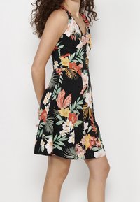 Vestido negro floral con cuello en V, sin mangas, con patrones de hojas y flores tropicales en colores vibrantes. Detalle de falda acampanada.