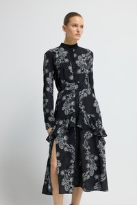 Schwarzes, langärmeliges Kleid mit weißem Paisley-Muster, ausgestelltem Saum, Knopfleiste vorne und seitlichem Schlitz, aus leichtem Stoff gefertigt.