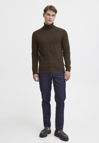 Pull en tricot marron à col roulé associé à un jean bleu foncé et des mocassins sombres. Le pull présente une coupe ajustée et des bords côtelés.
