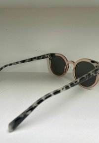 Lunettes de soleil rondes avec des montures en or rose et des branches à motifs noir et blanc. Verres foncés, design en plastique léger.