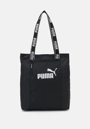 Czarna torba typu tote marki Puma z przednią kieszenią na zamek, białym logo Puma oraz czarnymi uchwytami z powtarzającym się białym napisem „PUMA”.