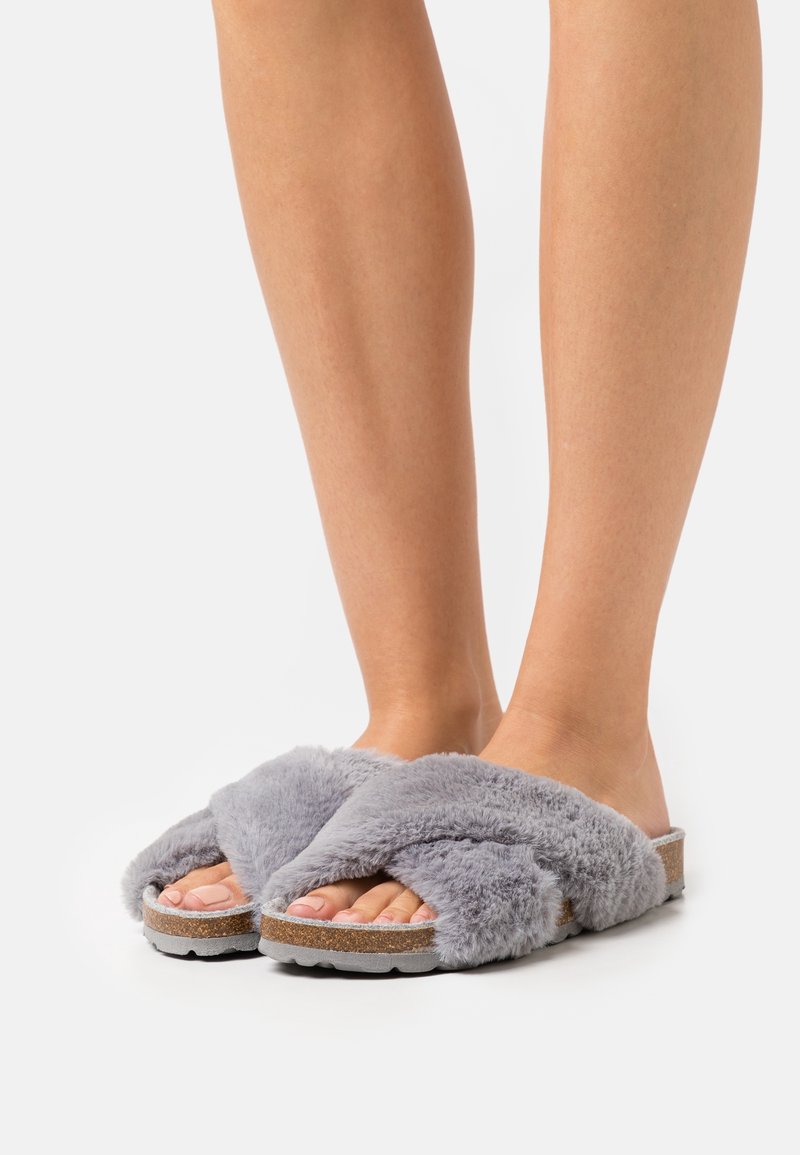 Sandales slide en peluche grises avec un design à lanières croisées. Semelle intérieure en liège et semelle texturée pour une meilleure adh érence. Matériau doux offrant confort.