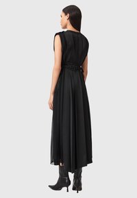 Abito maxi nero con design plissettato, vita aderente e dettagli legati. Presenta un collo alto e uno stile senza maniche, abbinato a stivali neri.