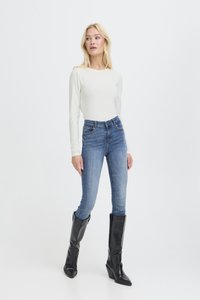 Top de manga larga color marfil combinado con jeans ajustados azules, complementado con botas de cuero negras hasta la rodilla con tacón grueso.