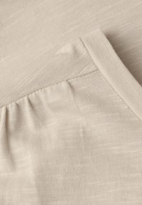 Close-up of beige ribbed knit fabric with gathered seam detail on a soft textile surface.