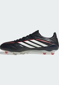 Chaussure de football noire avec des accents blancs et rouges. Présente un design élégant, une tige synthétique texturée, et des crampons transparents avec des pointes rouges.
