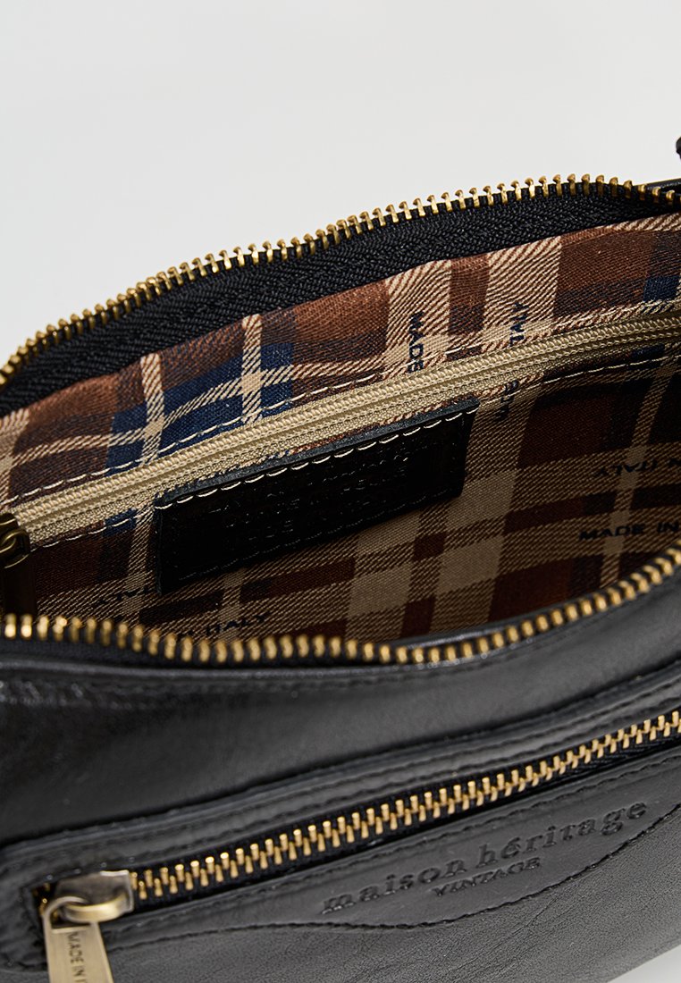 Wnętrze czarnej skórzanej torby z wypełnieniem w brązową i beżową kratkę, z złotymi zamkami błyskawicznymi i małą skórzaną metką.