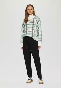 Overmaatse trui met groene en zwarte strepen op een witte achtergrond; gecombineerd met zwarte joggingbroek met trekkoord en witte sneakers met tan-kleurige zolen.