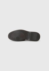 Black rubber shoe sole with circular patterns and ridged accents. Features a smooth texture and a defined heel area.