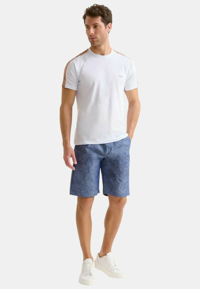 Outfit casual da uomo con una maglietta azzurro chiaro con dettagli marroni e pantaloni corti blu a fantasia, abbinati a sneakers bianche.