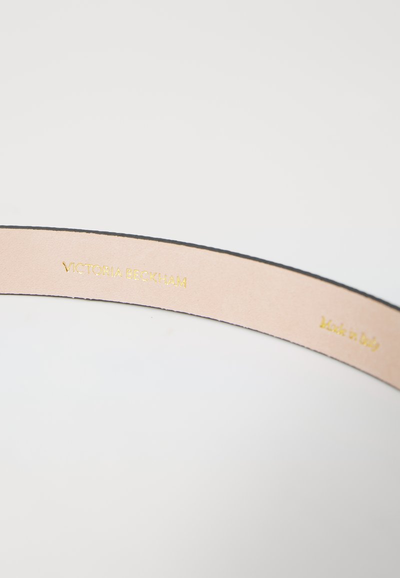 Læderinteriør i en taske med en glat beige finish, der har præget guldtekst, der siger "Victoria Beckham" og "Made in Italy."