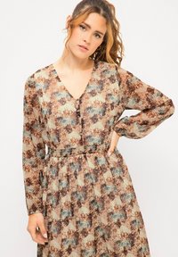 Langärmliges Kleid aus transparenter Stoff, mit V-Ausschnitt, braun-blauem abstraktem Muster und elastischem Taillenbund für eine figurschmeichelnde Silhouette.