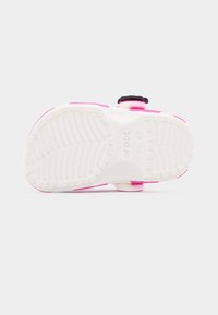 Semelle texturée blanche d'une sandale Crocs rose, montrant les motifs d'adhérence et la marque de taille sur un fond clair uni.