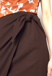 Brun texturerad kjol med en knuten midjedetalj. Tyget ser rynkigt ut och ger en flödande design runt höfterna.