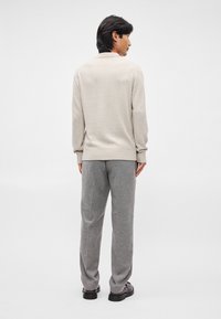 Pulover bej tricotat cu un finisaj texturat, asortat cu pantaloni gri deschis. Croială slim, mansete cu dungi și un design simplu. Pantofi negri.