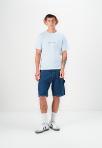 Light blue short-sleeve t-shirt with "JACK & JONES" logo, paired with blue denim shorts and gray sneakers, featuring white and black accents.