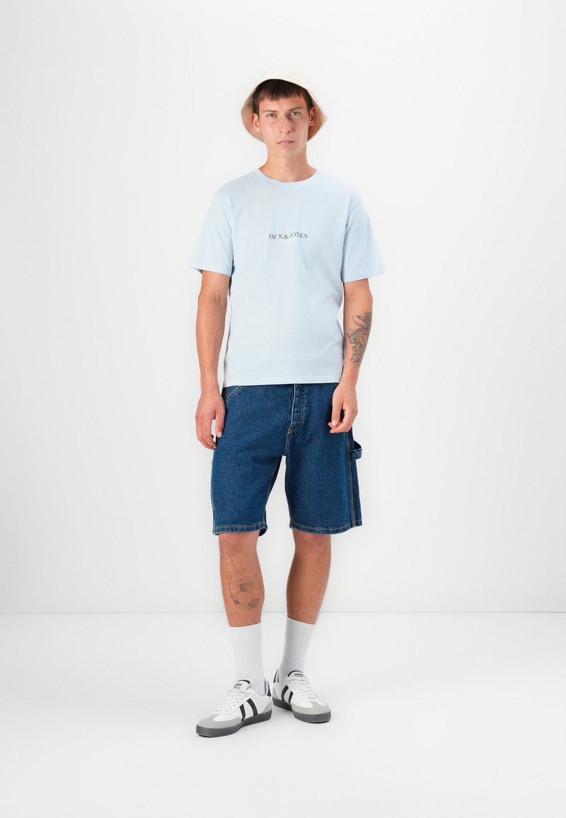 Light blue short-sleeve t-shirt with "JACK & JONES" logo, paired with blue denim shorts and gray sneakers, featuring white and black accents.