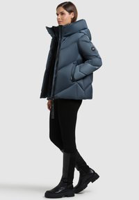 Pehmendusega tume sinine jope kõrge kraega, diagonaalse tikandmustriga, tõmblukuga ja kahe küljetaskuga. Kandmisel mustad retuusid ja saapad.