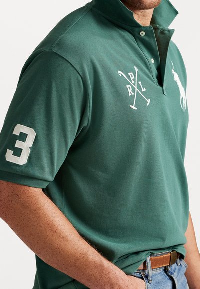 Zielona koszulka polo z wysokim kołnierzykiem, krótkim rękawem. Posiada biały haftowany logotyp "P.R.L" oraz skrzyżowane mallety polo, a na rękawie znajduje się biały numer 3.