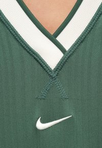 Πράσινη φανέλα με V-λαιμόκοψη, διακοσμημένη με λευκή ριμπ υφασμάτινη λαιμόκοψη. Ένα μικρό λευκό λογότυπο της Nike βρίσκεται κοντά στο κέντρο του κάτω μέρους.