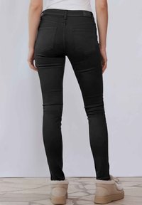 Vaqueros negros ajustados con una textura suave, que cuentan con dos bolsillos traseros y una cintura alta. Combinados con calzado de color claro, forrado de pelo.
