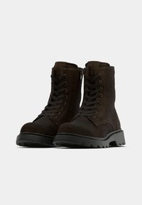 Brūni ādas potīšu zābaki ar šņorzolēm priekšpusē un sānu rāvējslēdzēju. Aprīkoti ar izturīgu gumijas zoli un teksturētu virsmu. Izstrādāti izturībai.