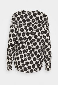 Blouse à manches longues avec un motif floral noir et blanc, poignets boutonnés et un détail plissé à l'arrière.