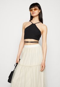 Top cropped preto com alças finas, apresentando um design justo. Combinado com uma saia branca translúcida, fluida e em camadas, e uma bolsa preta.