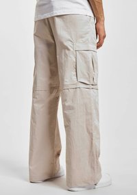 Pantalons cargo beiges avec une coupe ample, fabriqués en tissu léger, dotés de grandes poches latérales et d'une surface texturée.