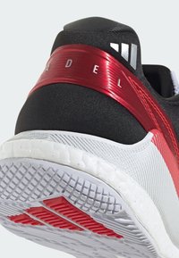 Baskets noires de sport avec une tige texturée, une bande d'accent rouge et une semelle blanche présentant un motif de semelle. Logo argenté sur le détail rouge.
