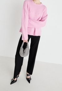 Pink fuzzy sweater with ribbed hem, black wide-leg trousers, and pointed black heels with buckle accents. Model holds a textured black-and-white handbag.
