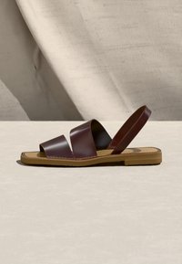 Καφέ δερμάτινο σανδάλι με δύο πλατιές λουρίδες πάνω από το πόδι και μία ενιαία λουρίδα πίσω στο ουδέτερο φόντο.