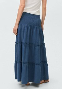 Long, tiered maxi skirt in dark blue, made of textured fabric with a smocked waistband. Features ruffled seams and a relaxed fit.