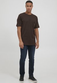 Kahvan lyhythihainen t-paita rintataskulla, yhdistetty tummansiniset slim fit -farkut ja mustat lenkkarit; yksinkertainen muotoilu, puuvillamateriaali.