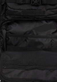 Czarna wnętrze plecaka z gładką fakturą tkaniny. Wiele przegródek, w tym siatkowa kieszeń oraz zamykana na zamek część do organizacji.