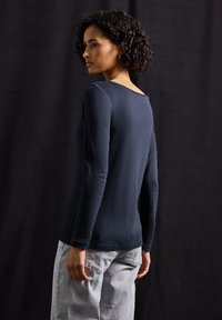 Marineblauwe langesleevetop met een brede halslijn, slim fit en zachte textuur. Gecombineerd met lichtgrijze denim jeans, gezien vanuit de achterkant.