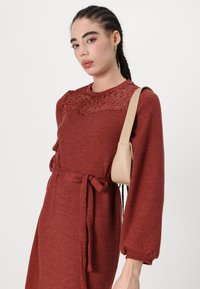 Rustfarget strikket kjole med blonde yoke, lange ermer og belte i livet. Glatt tekstur med ribbestrikket detaljering på mansjettene.