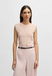 Ljust rosa ärmlös topp med ett strukturerat, chevronmönster. Kombinerad med vida, ljusrosa byxor och ett svart bälte.