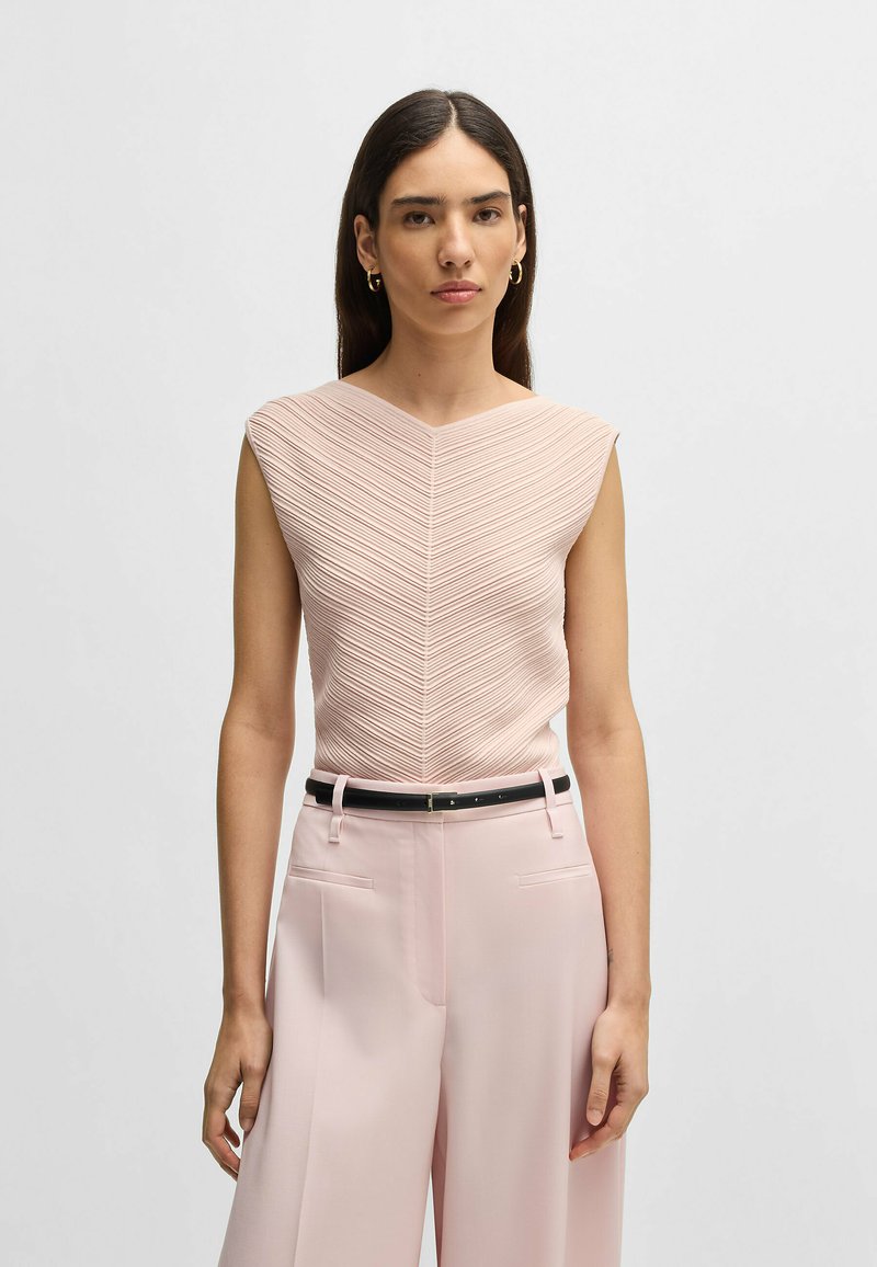 Ljust rosa ärmlös topp med ett strukturerat, chevronmönster. Kombinerad med vida, ljusrosa byxor och ett svart bälte.