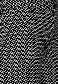 Svartvitt mönstrat tyg med ett upprepat abstrakt motiv, slät yta och synliga sömmar längs skarvarna.