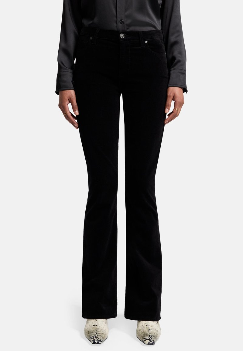 Jeans en velours côtelé noir à jambes évasées, avec un design à cinq poches, fermeture à bouton à l'avant et tissu texturé, associés à des bottes pointues de couleur claire.