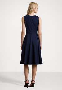 Vestido sem mangas azul marinho com corpete ajustado e saia rodada. Apresenta um fecho nas costas e um tecido liso e texturizado.