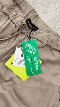 Beige fabric with a soft, textured appearance. Two tags: green EcoVero tag and a smaller white tag, both attached with black strings.